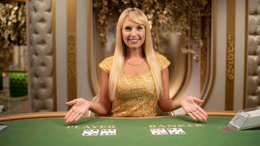 Smiling baccarat dealer in golden dress.